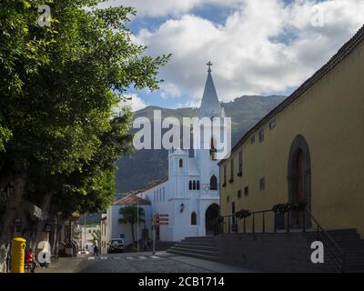 Spanien, Kanarische Inseln,Teneriffa, Los Silos, 19. Dezember 2017: Weiße Kirche und historische Gebäude in einem alten Dorf mit grünen Bäumen und Hügeln Stockfoto