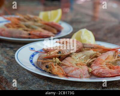 Nahaufnahme gekochte Riesengarnelen mit Zitrone und Knoblauch Auf dem Teller auf dem Marmortisch Stockfoto