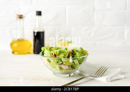 Frisch hausgemachter Salat aus Salat, Gurke, Rettich und gekochten Eiern in einer Glasschüssel auf einem weißen Holztisch. Olivenöl und Sojasauce zum Dressing. Stockfoto