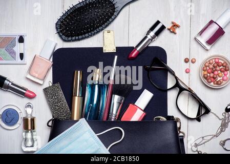 Chirurgische Gesichtsmaske mit verschiedenen Make-up und kosmetische Produkte fallen Aus einer weiblichen Tasche Tischplatte flach legen Stockfoto