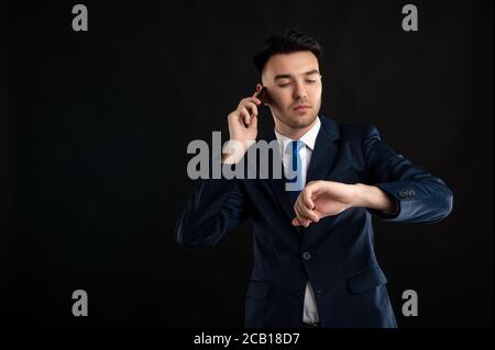 Portrait von wütend Business-Mann trägt blauen Business-Anzug und Krawatte reden am Telefon, Blick auf seine Uhr isoliert auf schwarzem Hintergrund mit Kopierraum Stockfoto