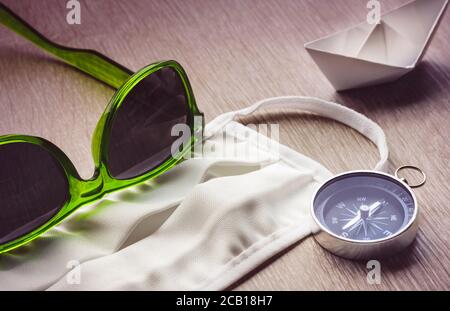 Sicheres Reisen, Stillleben. Chirurgische Maske und Kompass mit grüner Sonnenbrille und Papierschiff. Stockfoto