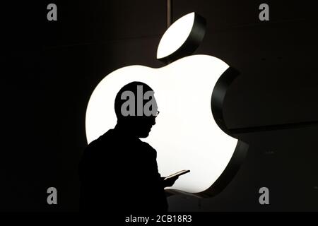 Hongkong - November, 2019: Silhouette einer Person, die das Handy vor dem Apple-Logo benutzt Stockfoto