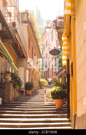 Sonnenaufgang auf der alten malerischen Straße in Bellagio City. Lombardei. Italien. Am frühen Morgen ohne Touristen. Frau geht auf die Treppe. Stockfoto