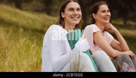 Glückliche Freundinnen, die nach einem Workout auf den Wiesen sitzen. Fitness-Frauen sitzen zusammen und entspannen sich nach einem Workout. Stockfoto