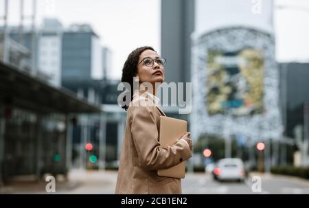 Geschäftsfrau mit einem digitalen Tablet, das über ihre Schulter schaut. Weibliche Geschäftsexpertin, die auf ihr Bürogebäude zurückblickt. Stockfoto