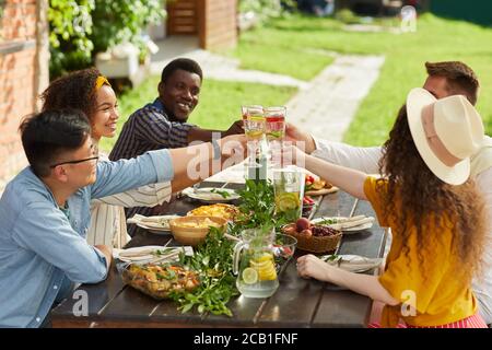 Multi-ethnische Gruppe von Freunden klirren Cocktail-Gläser, während im Sommer genießen Abendessen im Freien, kopieren Raum Stockfoto
