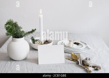 Traditionelle Weihnachts-Tischgestelle. Goldenes Besteck, Tannenzweige in Vase, Teller und brennende Kerze in keramischen Kerzenhalter auf Leinentisch Stockfoto