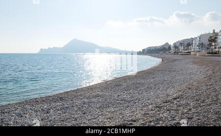 Steinstrand mit Blick auf die sonnige Altea City Küste und Berge, Costa Blanca, Spanien Stockfoto