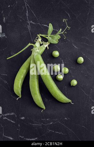 Frisch geerntete grüne Erbsen auf schwarzem Marmor von oben Stockfoto