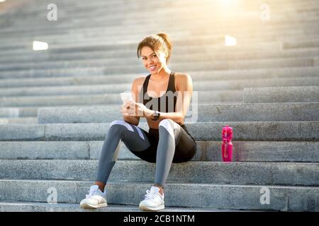 Afrikanische athletische Frau in Sportkleidung mit Telefon während der Ruhe Stockfoto