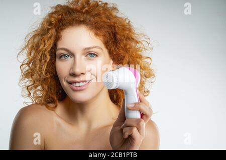 Freudige junge Frau hält Reinigung Gesichtsbürste Stockfoto