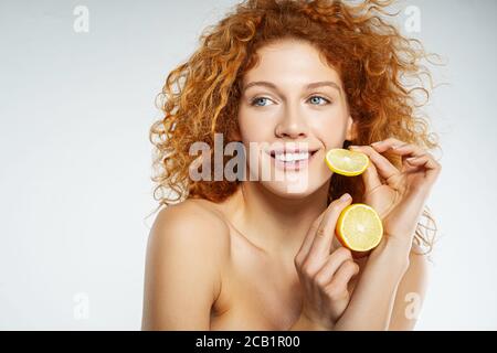 Charmante junge Frau mit roten lockigen Haaren hält frische Zitrone Stockfoto
