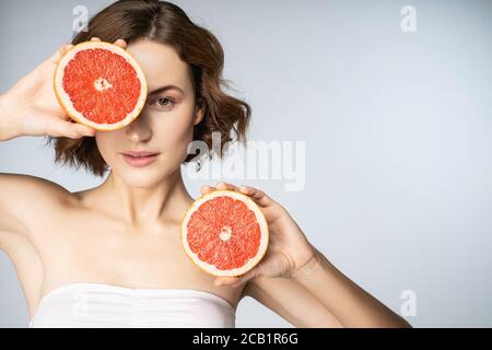 Attraktive junge Frau mit perfekter Haut hält Grapefruit Hälften Stockfoto