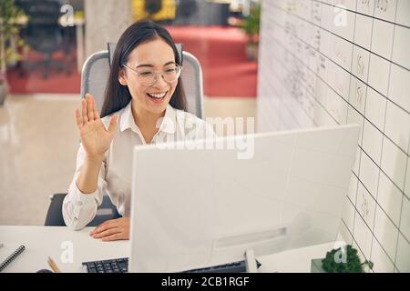 Positiv erfreut junge weibliche Person winkt ihre Hand Stockfoto