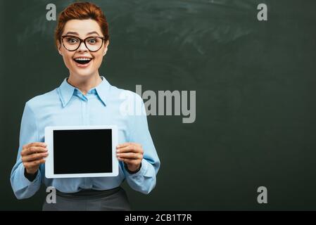 Aufgeregt Lehrer zeigt digitale Tablette mit leerem Bildschirm in der Nähe Kreidetafel Stockfoto