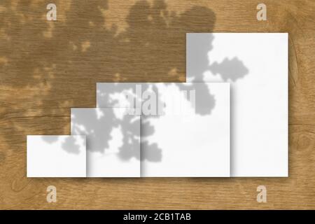 Mehrere horizontale und vertikale Blätter aus weißem strukturiertem Papier vor einem Holztisch Hintergrund. Mockup mit einer Überlagerung von Pflanzenschatten. Natürlich Stockfoto