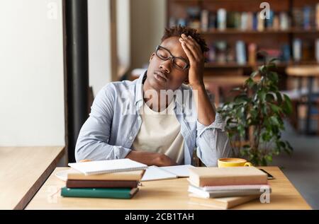 Afroamerikanischer Kerl mit Büchern erschöpft von Studium oder Arbeit Im städtischen Café Stockfoto