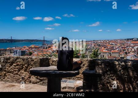 Lissabon, Portugal, Mädchen, das mit gekreuzten Beinen auf einem Steintisch in den Gärten des Castelo de San Jorge sitzt. Teenager verbringt ihre Zeit allein, nachdenkliche Mädchen. Stockfoto