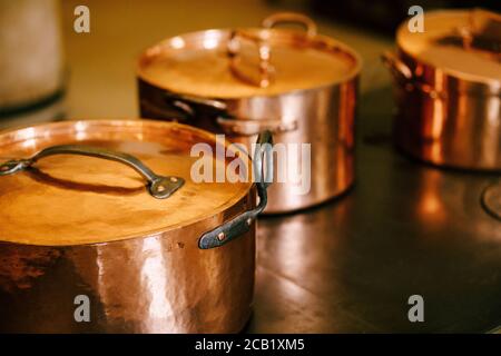 Drei Kupfertöpfe mit geschlossenen Deckeln auf einer Metalloberfläche. Stockfoto