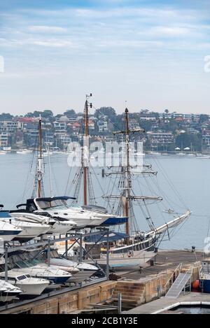 Ein Tall Ship ist neben einem doppelten Höhenlager vertäut Rack voller großer Motorcruiser auf Cockatoo Island in Sydney Harbour Stockfoto