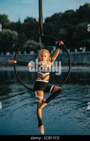 Kind Mädchen Aerialist führt akrobatische Elemente in hängenden Luftreifen vor dem Hintergrund von Fluss und Bäumen. Stockfoto