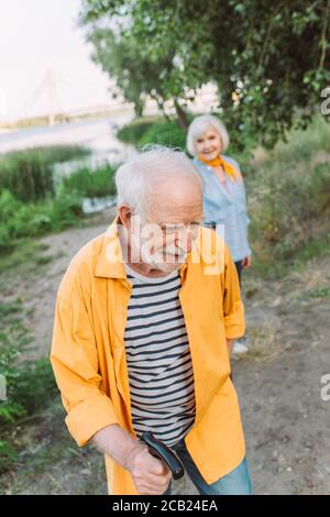 Selektiver Fokus auf lächelnden älteren Mann mit Gehstock in der Nähe Frau im Park Stockfoto