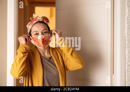 Portrait ofpositiv schwarze brasilianische Frau, die Maske auf ihr Gesicht legt und auf die Kamera schaut. Am Hauseingang. Mode, Individualität, Trend, Identität, Coron Stockfoto