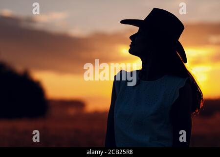 Frau Farmer Silhouette in Cowboy Hut bei landwirtschaftlichen Feld auf Sonnenuntergang Stockfoto