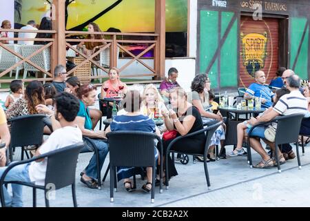 Punta Umbria, Huelva, Spanien - 7. August 2020: Die Leute, die auf der Terrasse eines Cafés und einer Bar in der Straße calle Ancha von Punta Umbria sitzen, tragen Protecti Stockfoto