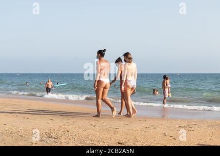 Punta Umbria, Huelva, Spanien - 7. August 2020: Frauen, die am Strand spazieren, tragen schützende oder medizinische Gesichtsmasken. Neue Normalität in Spanien mit sozialen DIS Stockfoto