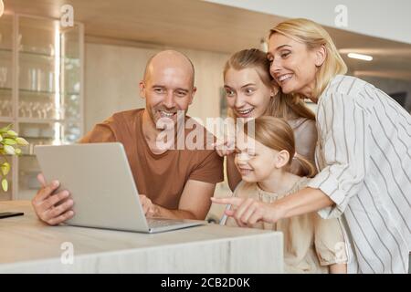 In warmen Farben Porträt von glücklichen modernen Familie mit Laptop zusammen, während im Video-Chat mit Verwandten in gemütlichen Innenraum, Kopierer Raum sprechen Stockfoto