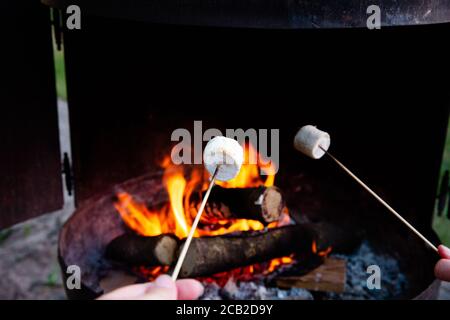 Der Mensch, der über dem Feuer röstet, flammt die Marshmallows über dem Lagerfeuer in der Nacht auf den Sommertag, für die Smores oder den Imbiss Stockfoto