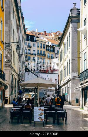 Café und Restaurant im belebten historischen Zentrum Baixa District. Perspektivischer Blick auf die Straße von Geschäften und Cafés in traditionellen alten Gebäuden Stockfoto