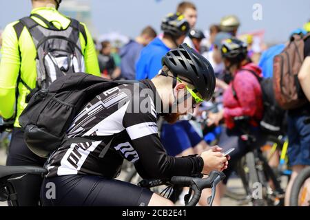 Dnipro Stadt, Ukraine 26 05 2019. Ein junger Mann sitzt in einem Helm auf einem Fahrrad und schaut in ein Smartphone. Radfahren, Sportveranstaltung in Dnepr. Stockfoto