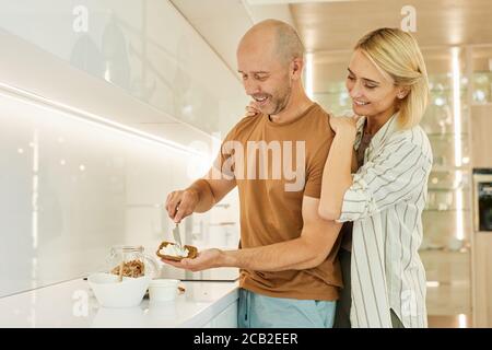 Warm-toned Taille up Porträt von glücklichen Erwachsenen Paar Kochen gesundes Frühstück zusammen, während in der modernen Küche Innenraum, kopieren Raum stehen