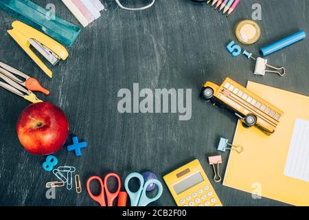 Draufsicht auf Rahmen mit Schulbus-Modell, reifen Apfel und Schulpapiere auf schwarzer Kreidetafel mit Kopierfläche Stockfoto