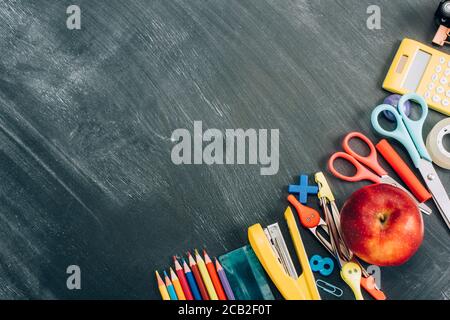 Draufsicht auf reifen Apfel und Schulpapiere auf schwarz Schwarzes Brett mit Kopierraum Stockfoto