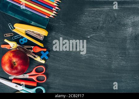 Draufsicht auf Schulbedarf und reifen Apfel auf schwarz Schwarzes Brett mit Kopierraum Stockfoto