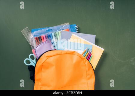 Draufsicht auf Schulrucksack mit Papeterie auf grüner Tafel Stockfoto