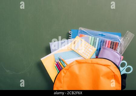 Draufsicht auf gelben Rucksack voller Schulbedarf auf Grüne Tafel Stockfoto