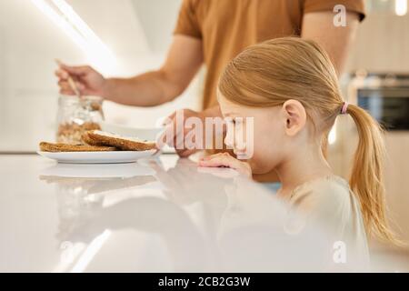 Seitenansicht Porträt von niedlichen kleinen Mädchen Blick auf leckere Sandwiches während der Wartezeit für das Frühstück in der Küche, kopieren Raum Stockfoto
