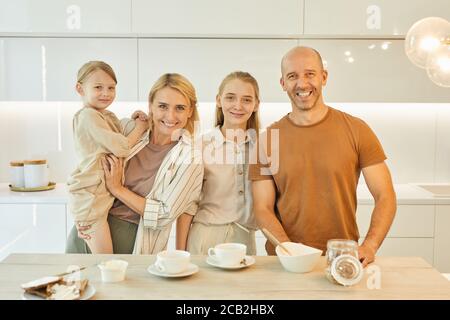 Warm-getönte Taille up Porträt der modernen glücklichen Familie Blick auf die Kamera, während das Frühstück zusammen stehend am Tisch in minimaler Küche Innenraum, Kopierer Platz Stockfoto