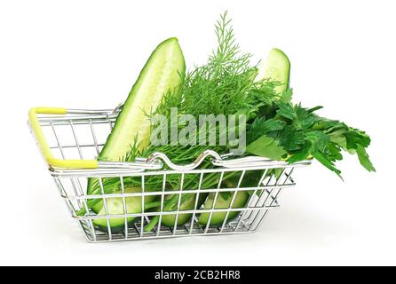 Ein kleiner Einkaufskorb mit Kräutern, Gurke, Tomate, Petersilie neben einem frischen, eingetopften grünen Salat auf weißem Grund. Gesunde Ernährung, vegetarische Kost, Stockfoto