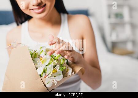 Beschnittene Ansicht der lächelnden Frau berühren Blumen in Blumenstrauß auf Bett Stockfoto