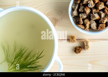 Hausgemachte Brühe aus Fleischknochen in einer Terrine mit Dill und Croutons auf einem hölzernen Hintergrund. Gesunde Ernährung Konzept. Paleo Diät. Nahaufnahme. Selektiver Fokus. Stockfoto