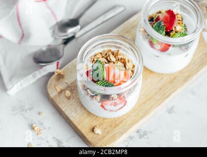 Zwei Gläser mit leckeren Parfaits aus Müsli, Erdbeeren und Joghurt auf weißem Marmortisch. Stockfoto