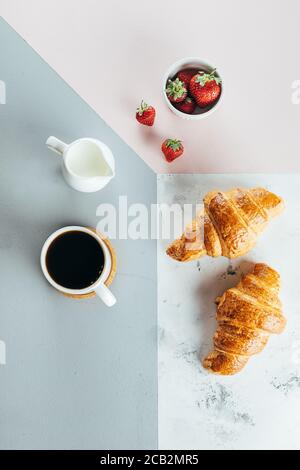 Gesundes Frühstück Morgen Konzept. Zwei Croissants, Schale mit Erdbeere und Tasse Kaffee über tricolor stilvoller Hintergrund, Draufsicht, flach liegend. Gesundheit Stockfoto