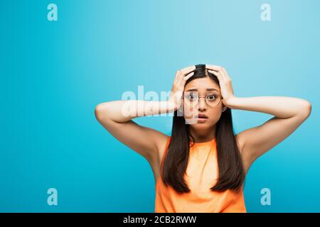 Schockiert asiatische Frau in Brille berühren Kopf auf blau Stockfoto