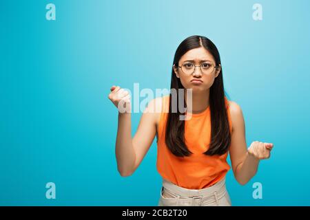 Frustriert asiatische Mädchen in Brille zeigt geballte Fäuste auf blau Stockfoto